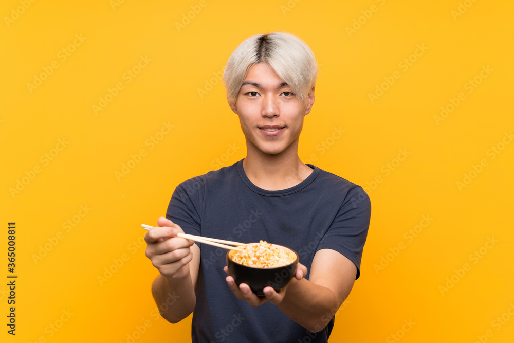 Young asian man with noodles over isolated yellow background Young asian man with noodles over isolated yellow background