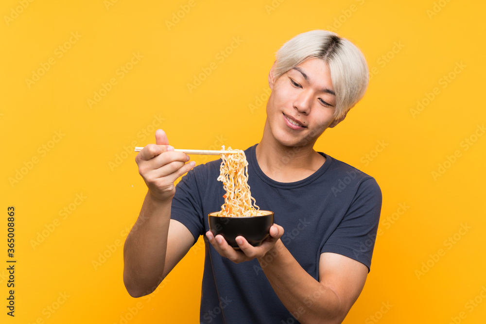 Young asian man with noodles over isolated yellow background Young asian man with noodles over isolated yellow background
