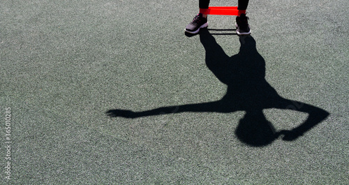 The shadow of a man in sneakers, with one arm bent closer to his head and the other pointing to the side. On the legs of the red ribbon for sports. The background of the Playground is green.