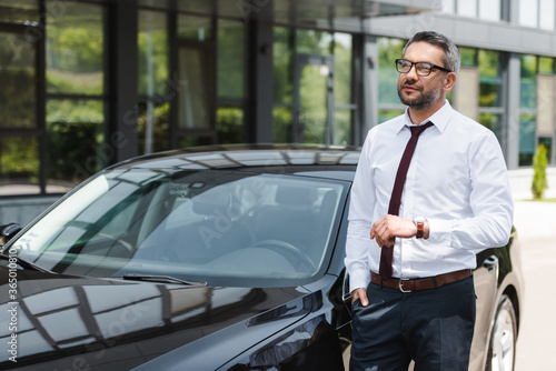 Handsome businessman with hand in pocket looking away near auto on urban street © LIGHTFIELD STUDIOS