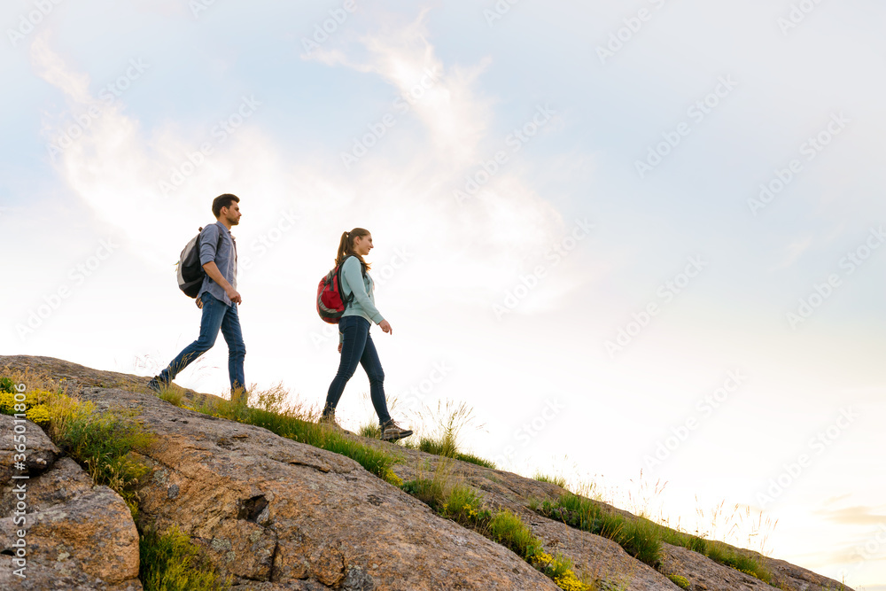 Couple of Young Happy Travelers Hiking with Backpacks on the Rocky Trail at the Evening. Family Travel and Adventure