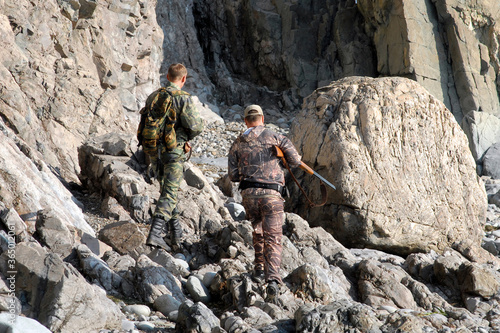 Two hunters (men) with shotguns on the rocky shore of the sea. Vicinity of Rudnaya Pristan town, Primorsky Krai (Primorye), Far East, Russia. photo