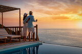 Ein Paar im Urlaub genießt den romantischen Sonnenuntergang über dem Meer bei einem Glas Wein am Pool