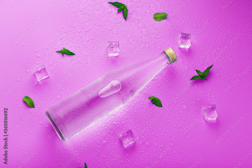 A bottle with an ice drink in drops of condensation, ice cubes and mint leaves on a pink background