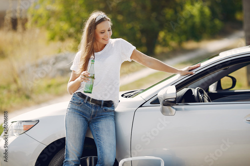 Woman by the car. Lady in a white t-shirt. Woman with bottle of water. Famale use the refrigerator.