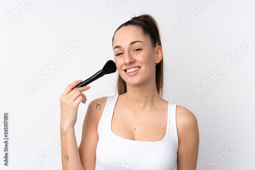 Young brunette woman over isolated white background holding makeup brush and whit happy expression
