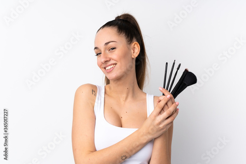 Young brunette woman over isolated white background holding makeup brush and whit happy expression