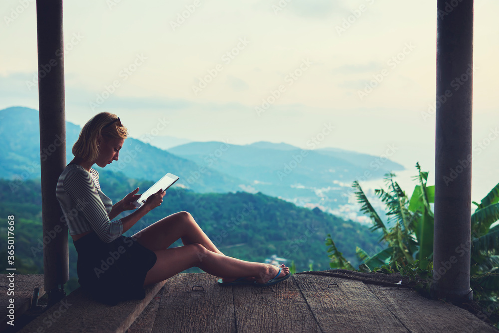 Young female freelancer is working in network via touch pad, while is sitting against beautiful view background with copy space for your advertising text message during her unforgettable trip in Asia