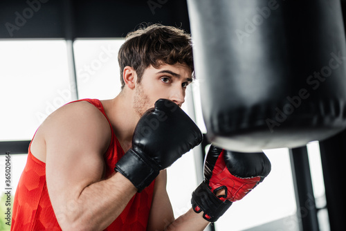 selective focus of sportsman in boxing gloves exercising with punching bag