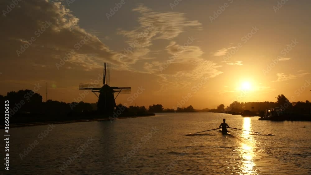 Sunrise over river near a Dutch windmill with a rower on the water Sunrise over river near a Dutch windmill with a rower on the water