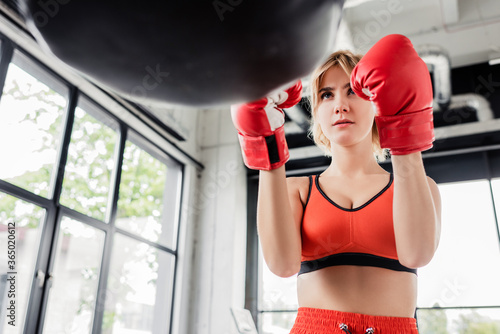 selective focus of young sportswoman in boxing gloves looking at punching bag