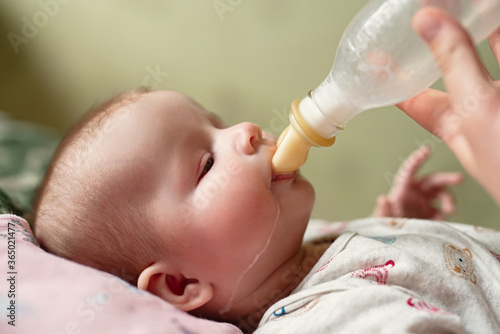 newborn baby eats milk from bottle, drops of food run down  cheek, dad gives baby  mixture