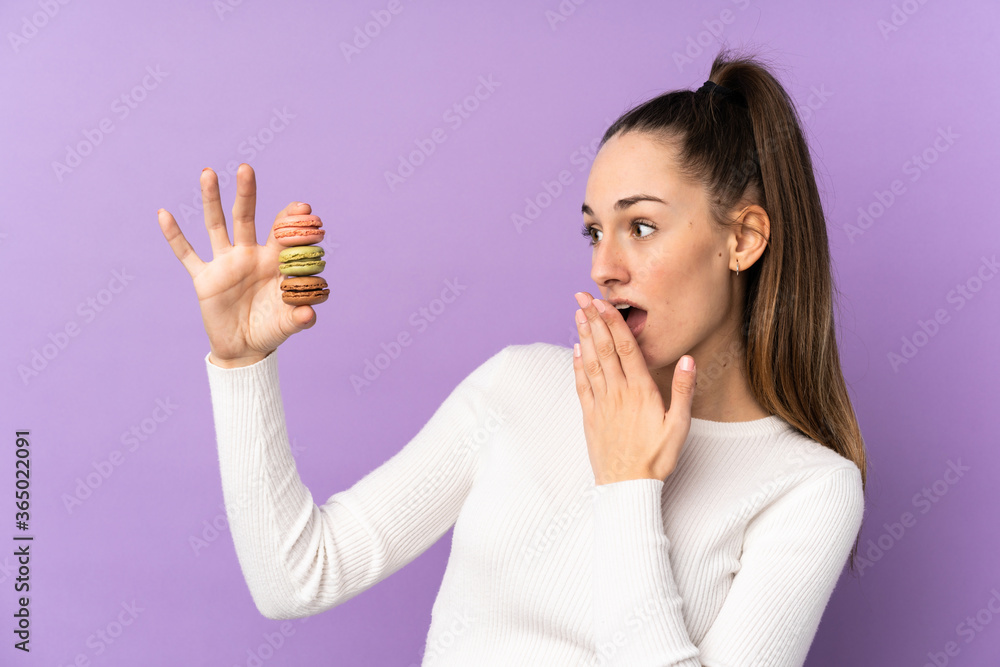 Young brunette woman over isolated purple background holding colorful French macarons and with surprise expression Young brunette woman over isolated purple background holding colorful French macarons and with surprise expression