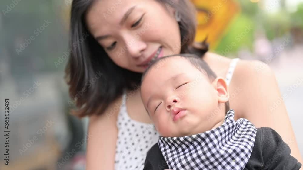 Asian mother smiling with her 8 months old baby boy sleeping on her, in park outdoor. Asian mother smiling with her 8 months old baby boy sleeping on her, in park outdoor.