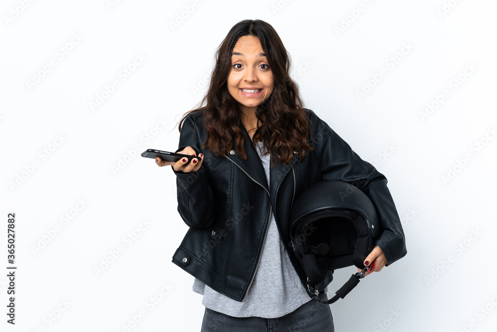 Young woman holding a motorcycle helmet over isolated white background keeping a conversation with the mobile phone with someone Young woman holding a motorcycle helmet over isolated white background keeping a conversation with the mobile phone with someone