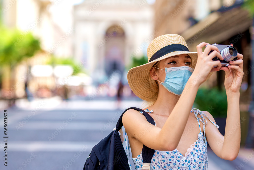 eautiful woman wearing face mask for prevention and holding camera in her hand while exploring the city