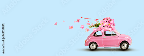 Pink car with bouquet of flowers on a roof on blue background. Copy space.
