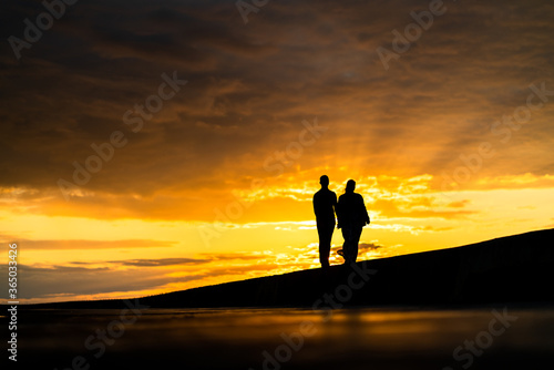 Silhouette of a couple enjoying beautiful golden sunset at the seaside  