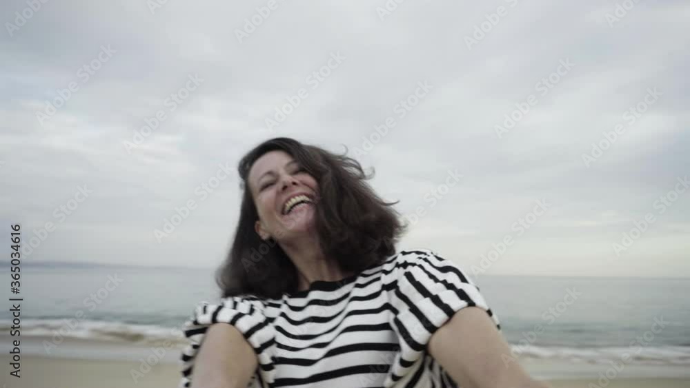 Brunette beautiful woman holding hands and swinging around on beach and looking at camera. Happy lady smiling and laughing. Sea waves flowing on background. Fun, seashore and weekend concept Brunette beautiful woman holding hands and swinging around on beach and looking at camera. Happy lady smiling and laughing. Sea waves flowing on background. Fun, seashore and weekend concept
