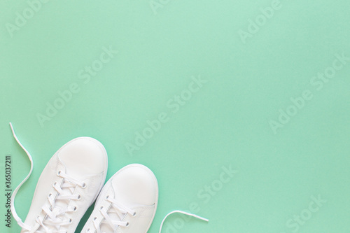 All white sneakers on mint green background. Top view, flat lay