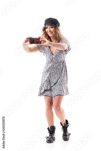 Happy laughing young woman taking photos or recording videos with smart phone. Full body length isolated on white background. 