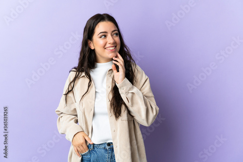 Young caucasian woman isolated on purple background looking up while smiling