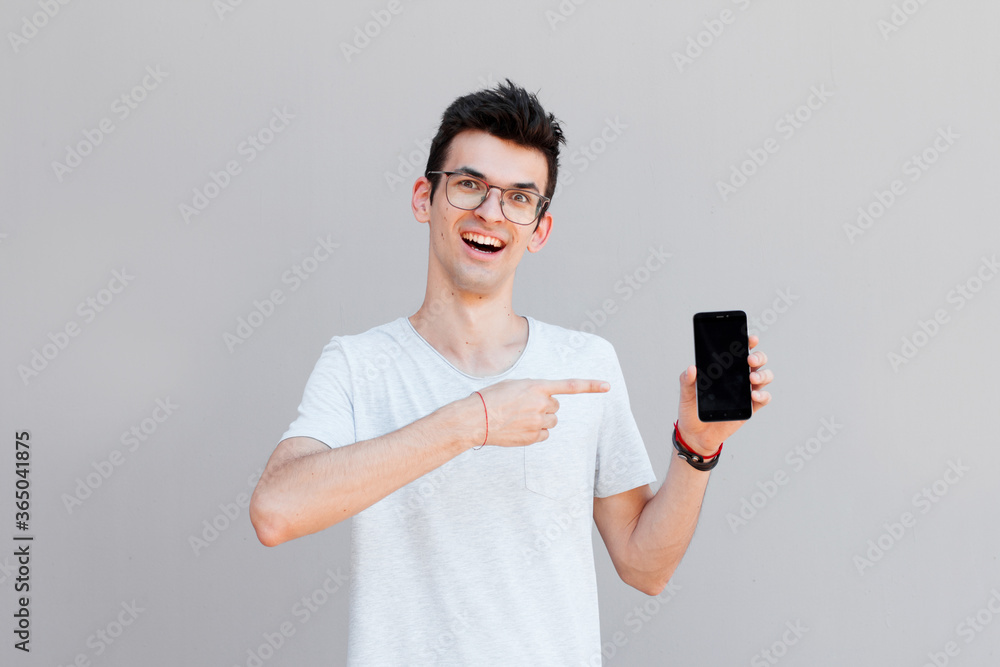 Portrait of a cheerful young man wearing casual clothing isolated over grey background, showing blank screen mobile phone Portrait of a cheerful young man wearing casual clothing isolated over grey background, showing blank screen mobile phone