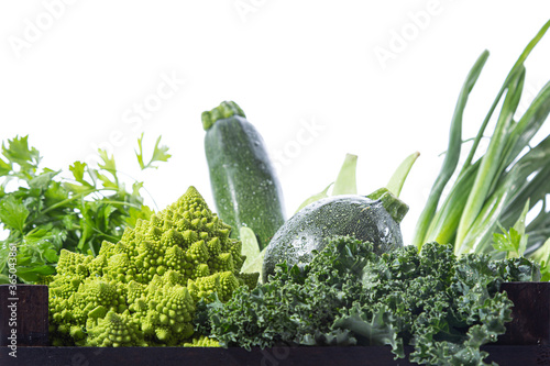 Close up view of variety of fresh green vegetables in a wooden box, isolated on white background.