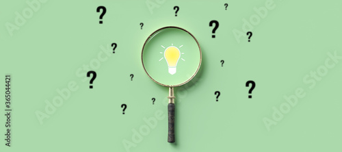magnifying glass with lightbulb as symbol for finding a solution on light green background photo