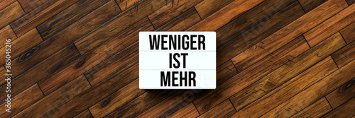 lightbox with German message for LESS IS MORE on wooden background