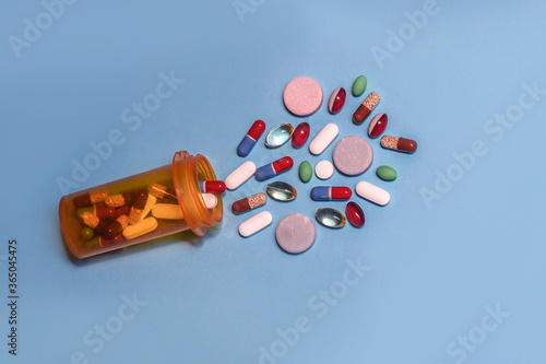 Orange prescription pill bottle isolated with color pills spilling on blue background