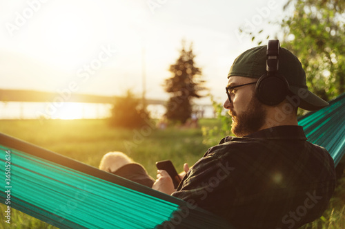 Closeup portrait from behind of melancholic bearded male hipster in eyeglasses and wireless headphones at sunset