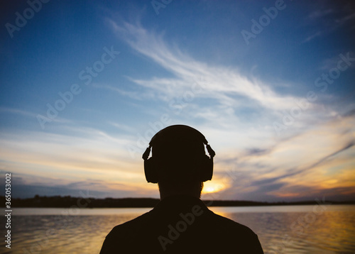 Closeup silhouette of man head in headphones at sunset by the lake