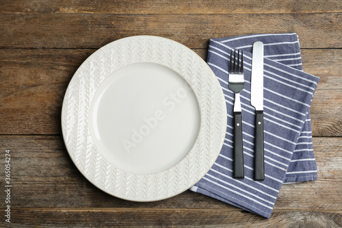 Empty ornate plate with cutlery and napkin on wooden table, flat lay