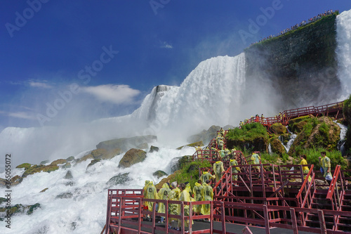 Niagara Falls, NY: Tourists in yellow raincoats enjoy the Cave of the Winds, stairs and platforms at the foot of the American Falls, on Goat Island.