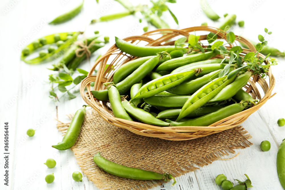 Green pea pods in basket on white wooden table Green pea pods in basket on white wooden table