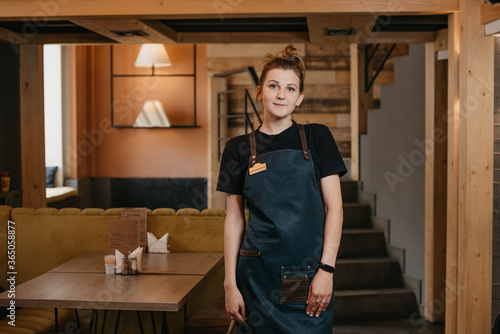 A young waitress is posing in a restaurant. A barista is preparing to work in a cafe.