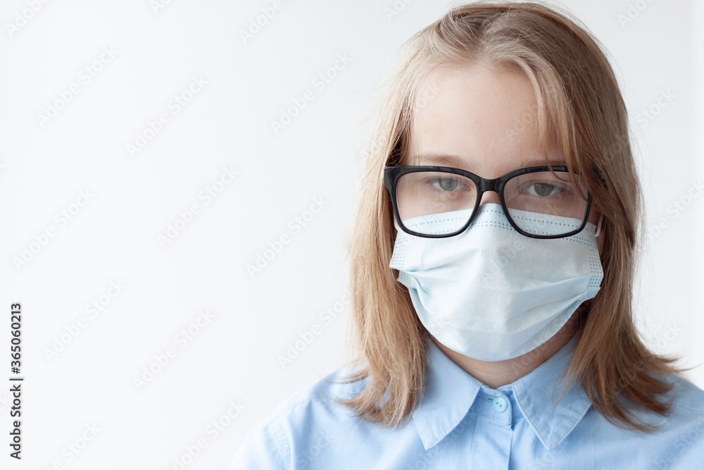 A teenage girl, blonde, in a blue shirt, a medical mask and glasses on a white background