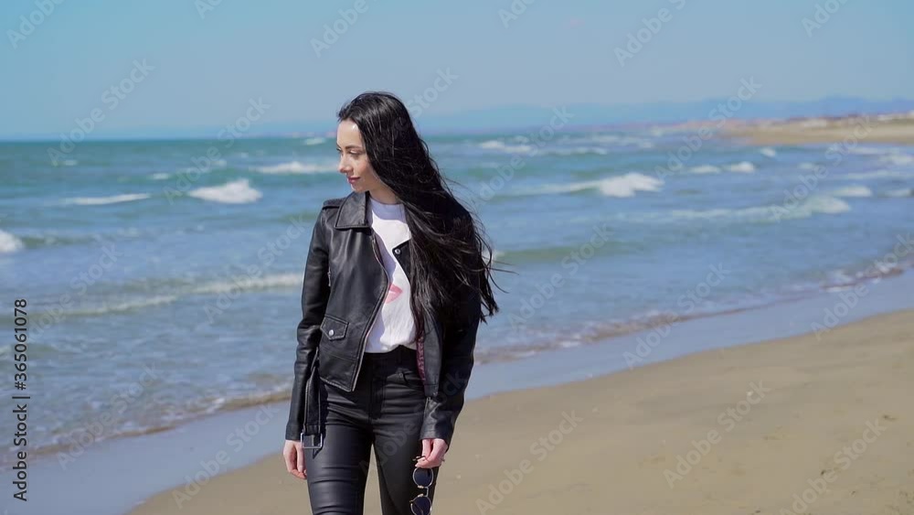 Portrait of a young stylish attractive girl walking or standing alone by the sea or ocean. Female with black hair in sunglasses sad dreams dreamy. The wind blows the hair. Beach. sea coast. Woman Portrait of a young stylish attractive girl walking or standing alone by the sea or ocean. Female with black hair in sunglasses sad dreams dreamy. The wind blows the hair. Beach. sea coast. Woman