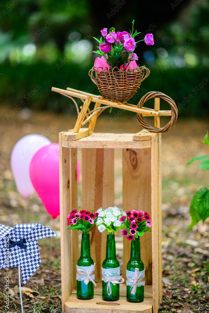 caixote de madeira três garrafas decoradas e uma carriola decoradas com  flores e ao fundo balões rosas com fundo natural verde Stock Photo | Adobe  Stock