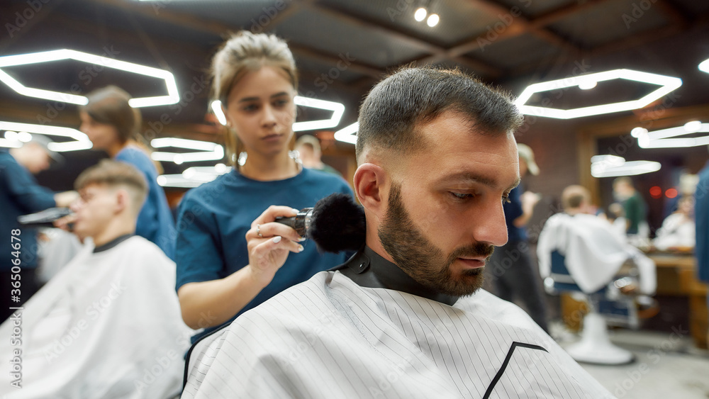 Young professional barber girl cleaning neck of a handsome bearded man after hair cutting. People visiting barbershop or beauty salon Young professional barber girl cleaning neck of a handsome bearded man after hair cutting. People visiting barbershop or beauty salon