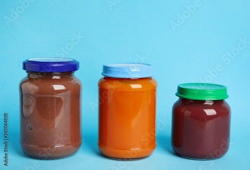 Healthy baby food in jars on light blue background