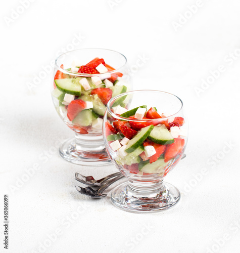Berry and vegetable salad of strawberries and cucumber with feta cheese in a glass on a light background. 
