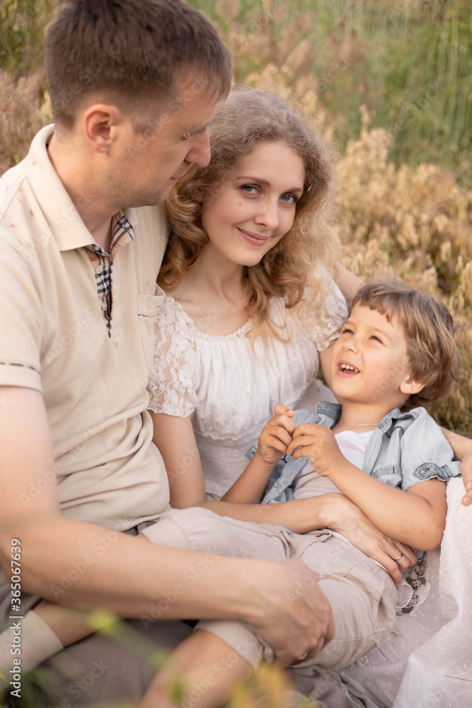 Happy family, cuddling in the field, mom and dad love their son, baby with golden hair, blonde woman, beautiful people, games with parents, bright children