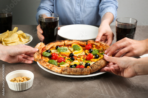 Women taking slices of delicious vegetable pizza at grey table, closeup