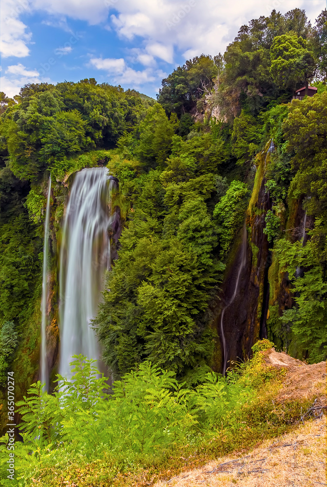 A long exposure view of the top waterfalls at Marmore, Umbria, Italy dropping vertically amongst the lush greenery in summer