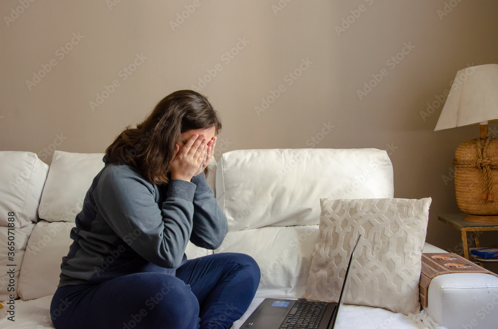young woman sitting on a white sofa working on a laptop using comfort clothes face palming