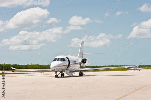 front view, far distance of a private jet plane loading before take off, from a tropical airstrip, on sunny day,