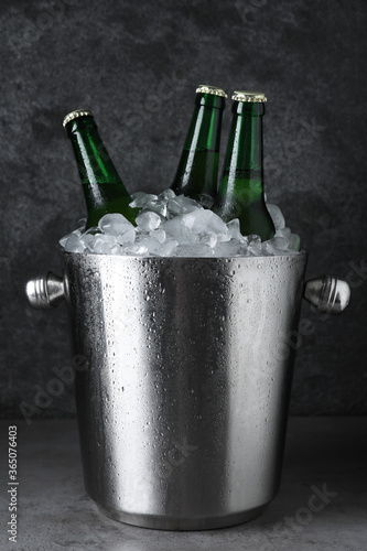 Metal bucket with beer and ice cubes on grey table