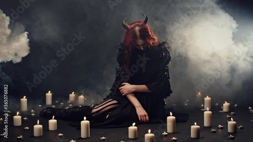 Horned witch spelling, conducting ritual and summon supernatural powers. Candles placing around female demon, smoke rising in the dark. Cult of devil, halloween party or halloween costume concept
